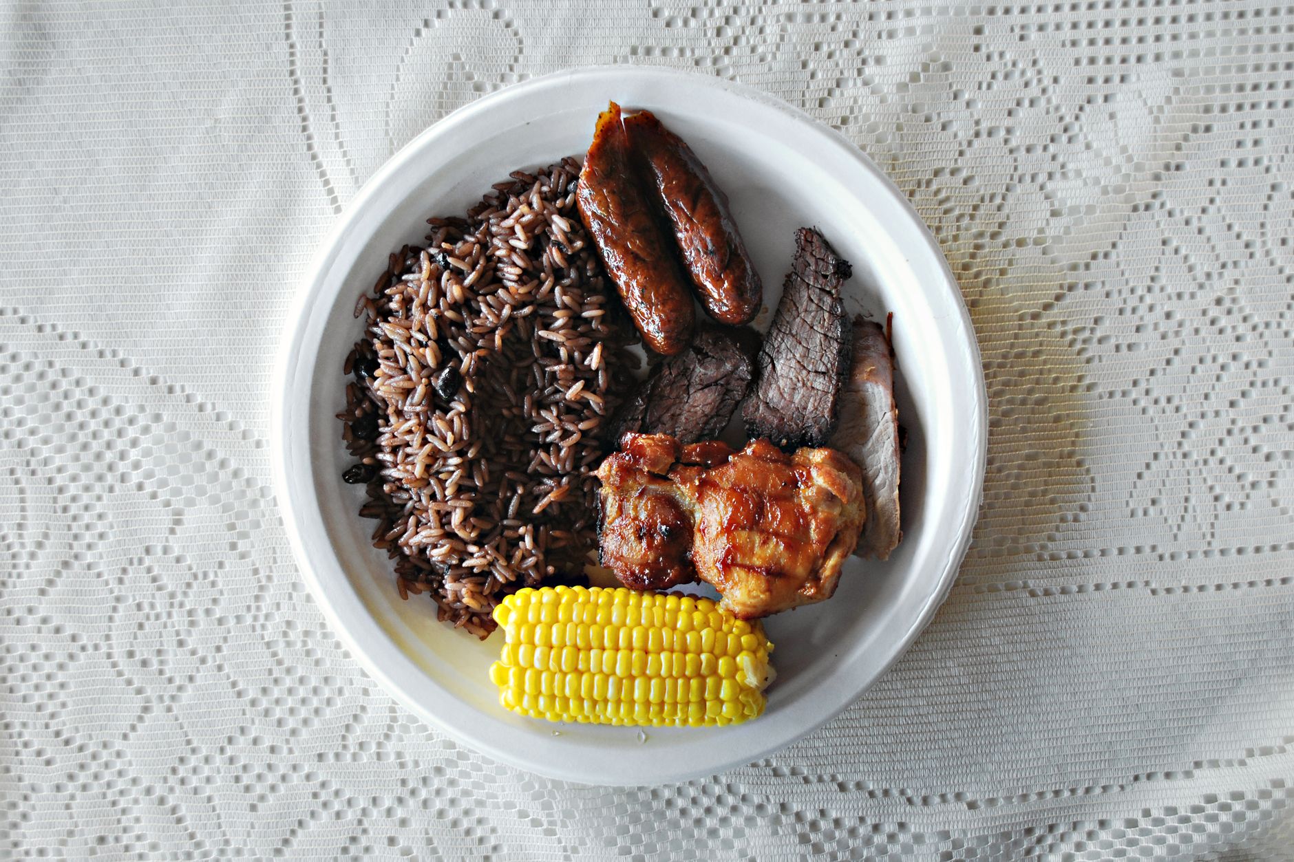 A platter of grilled meat served with rice and corn on a tablecloth