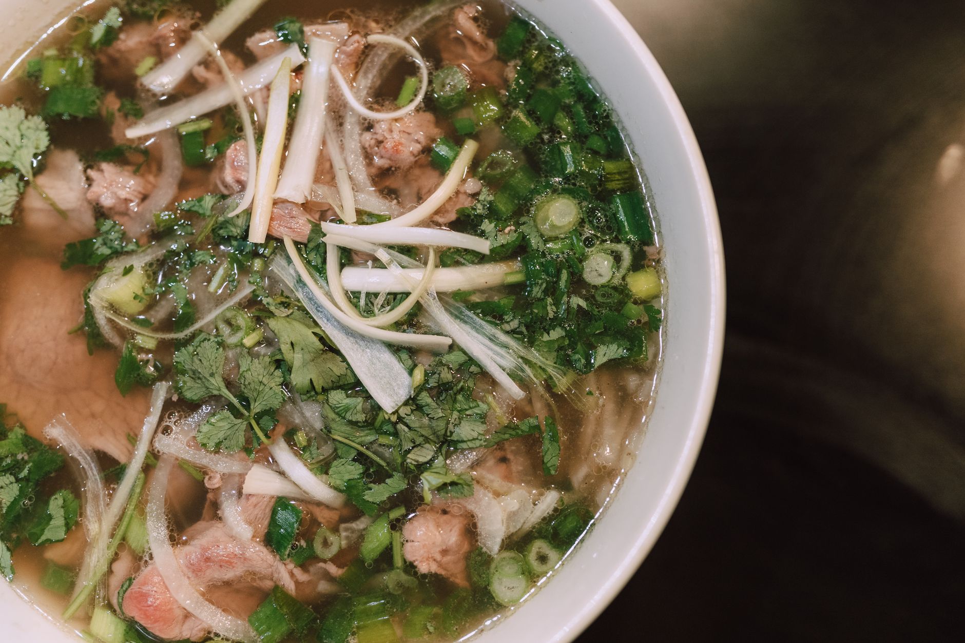 Bowl of Vietnamese pho noodle soup with fresh herbs and beef