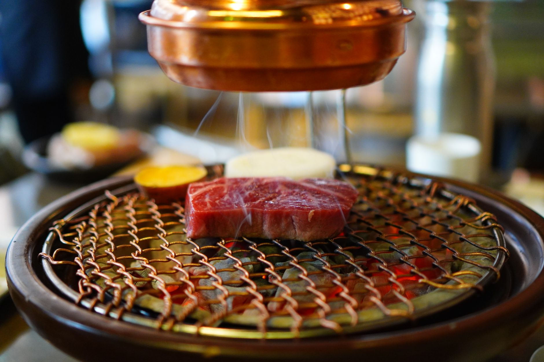 Raw beef sizzling on a Korean BBQ grill under a copper hood