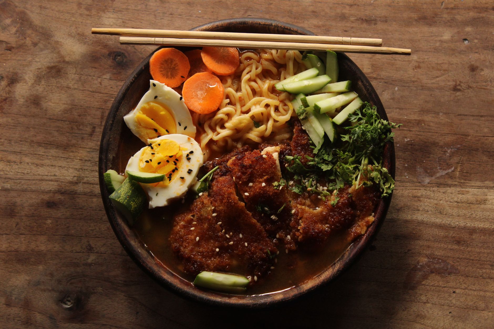 Close-up of a ramen bowl with egg, pork katsu and fresh vegetables